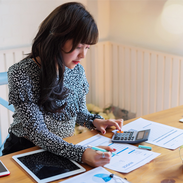 woman sitting at desk reviewing documentation and making calculations